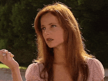 a woman with long red hair is wearing a pink top and a ring on her finger