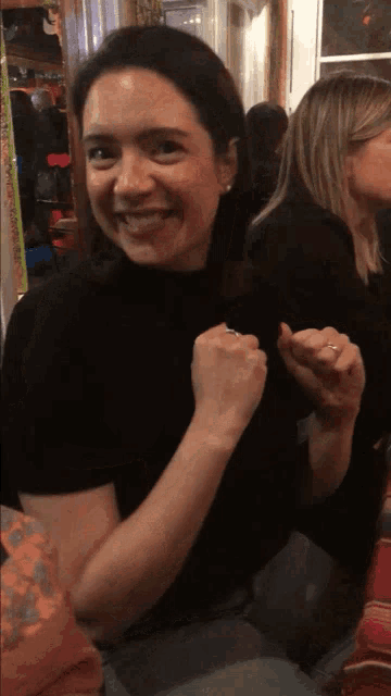 a woman wearing a black turtleneck is smiling and holding her fist up