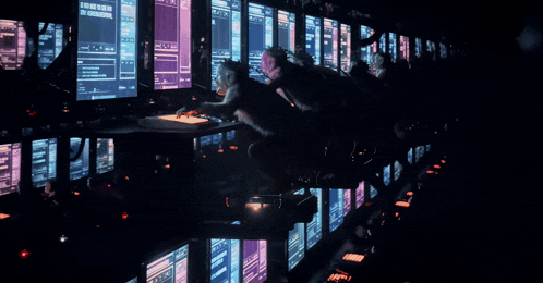 a group of people sitting in front of a row of computer monitors one of which says " the genesis "