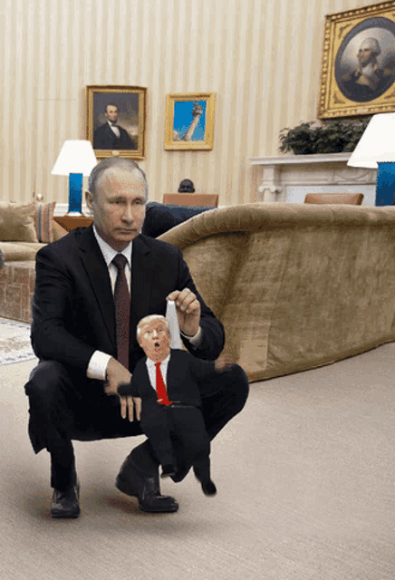 a man in a suit and tie squatting down holding a trump doll