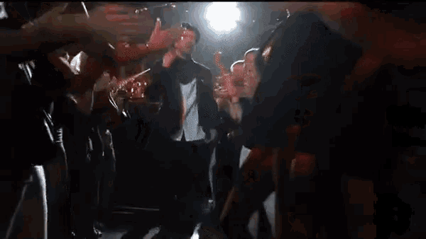 a group of people are dancing in a dark room with a man standing in the middle