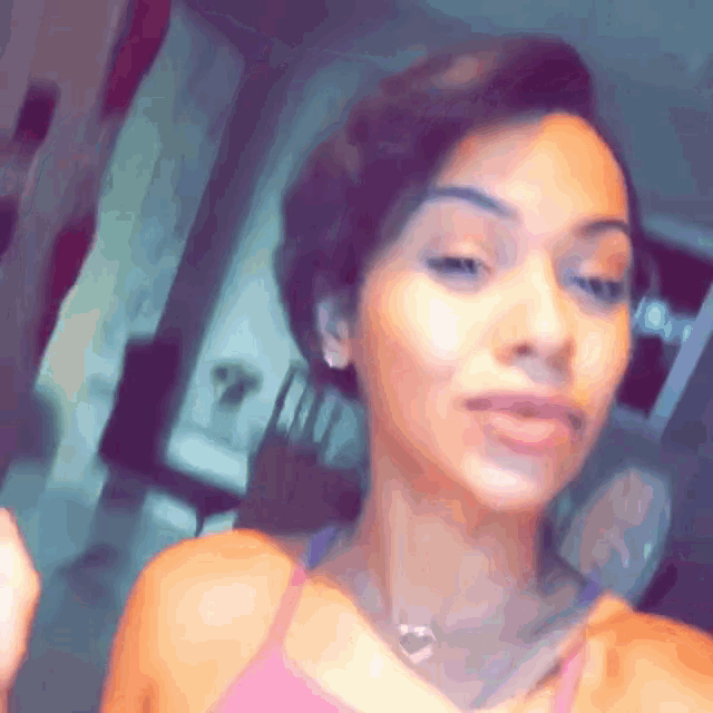 a woman wearing a pink tank top and a heart necklace