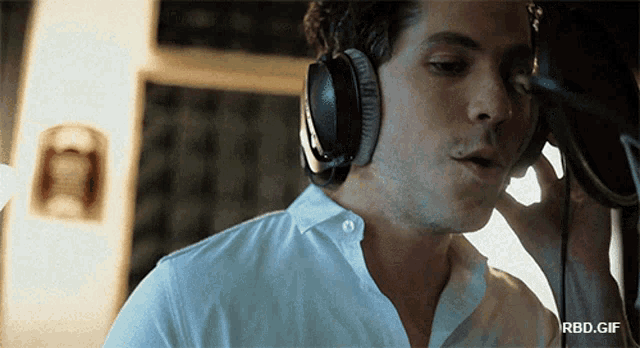 a man wearing headphones is singing into a microphone with a rbd.gif below him