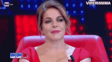 a woman in a red dress is sitting in a red chair on a tv show .