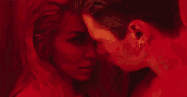 a man and a woman are kissing in front of a red curtain in a dark room .