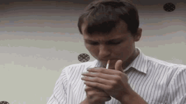 a man in a striped shirt is lighting up a cigarette