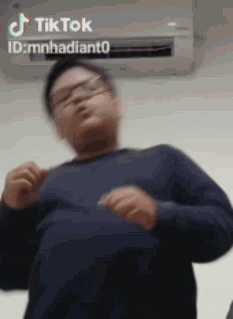 a man wearing glasses is dancing in front of an air conditioner with tiktok written on the bottom right