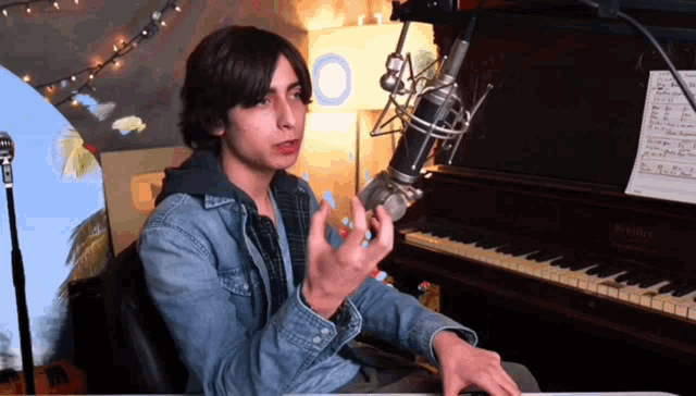 a man sitting in front of a piano with a microphone and a sheet of music on it