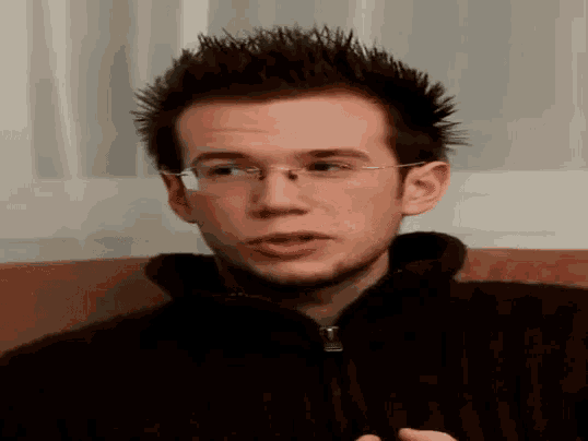 a young man wearing glasses is sitting on a couch