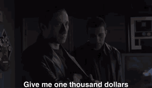 two men standing in a dark room with the words give me one thousand dollars on the screen