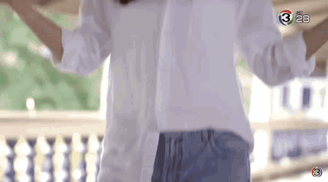 a woman in a white shirt and blue jeans is dancing on a balcony with the number 3 on the screen .