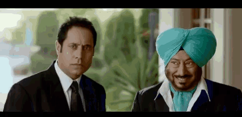two men in suits and turbans are standing next to each other and looking at each other .