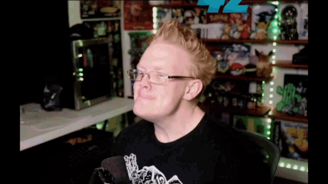 a man wearing glasses is sitting in front of a microphone in a room filled with toys
