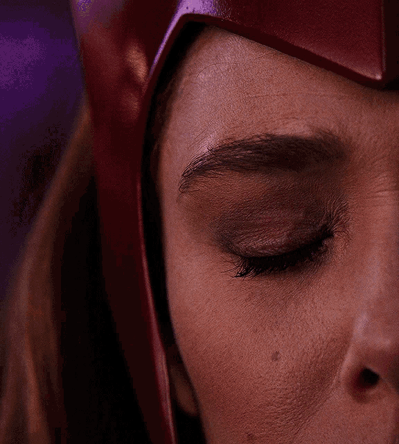 a close up of a woman 's red eye with a red helmet on