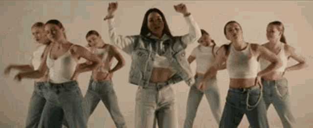 a woman in a denim jacket is surrounded by a group of women dancing .