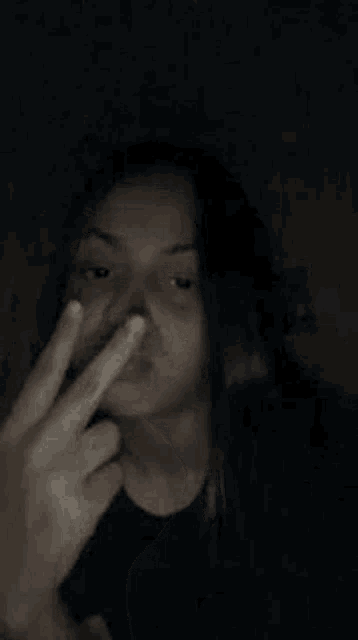 a woman with long hair is making a funny face with her hand on her chin in the dark .
