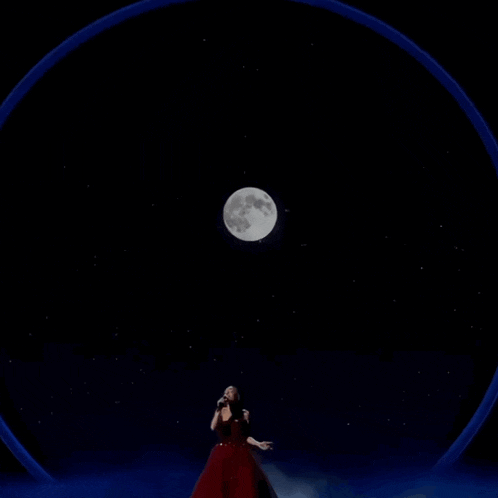 a woman in a red dress is standing in front of a full moon