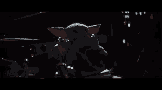 a baby yoda from star wars is sitting in the dark .