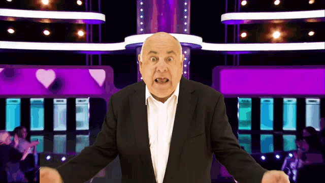 a bald man in a suit and white shirt stands in front of a purple background
