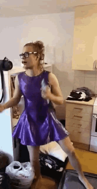 a woman wearing a purple dress and glasses is dancing in a kitchen