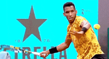 a man in a yellow shirt is playing tennis in front of a sign that says estrella 1876