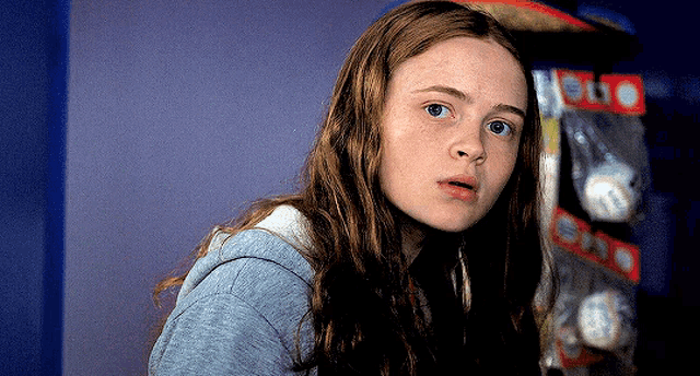 a girl with long hair is looking at the camera in front of a shelf that says hello