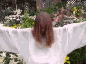 a woman in a scarecrow costume is standing in front of a flower bed .