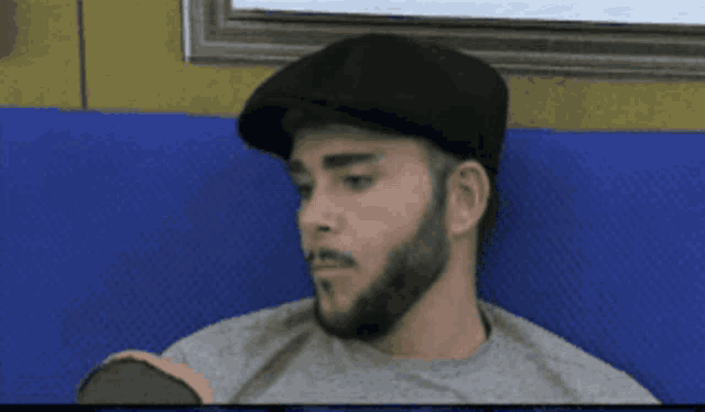 a man with a beard wearing a black hat and a grey shirt