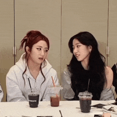 two women sitting at a table with a cup that says ' sherpa ' on it