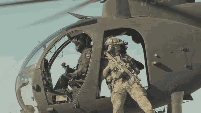 two soldiers in a military helicopter with one holding a rifle with the letter s on it