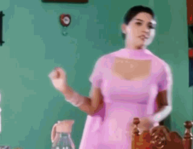 a woman in a pink dress is standing in a room with a green wall .