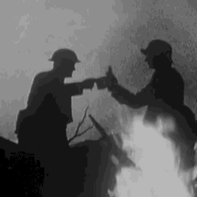 two soldiers are standing next to each other in front of a fire .
