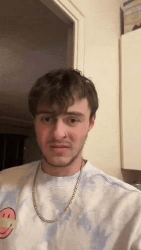 a man wearing a tie dye shirt with a smiley face on it and a chain around his neck