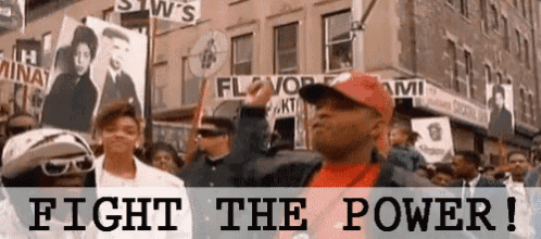 a man in a red hat is standing in front of a crowd holding a sign that says " fight the power "