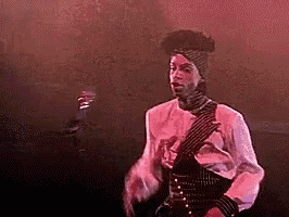 a man in a white shirt and black tie is dancing on a stage in a dark room .