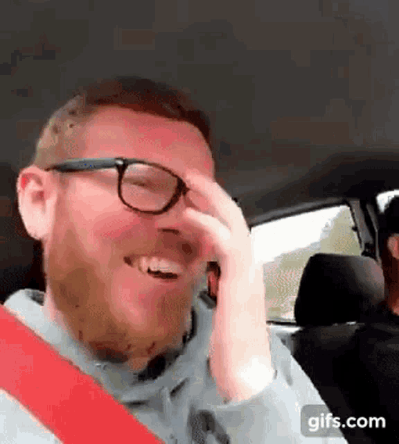 a man with glasses and a beard is laughing in a car .
