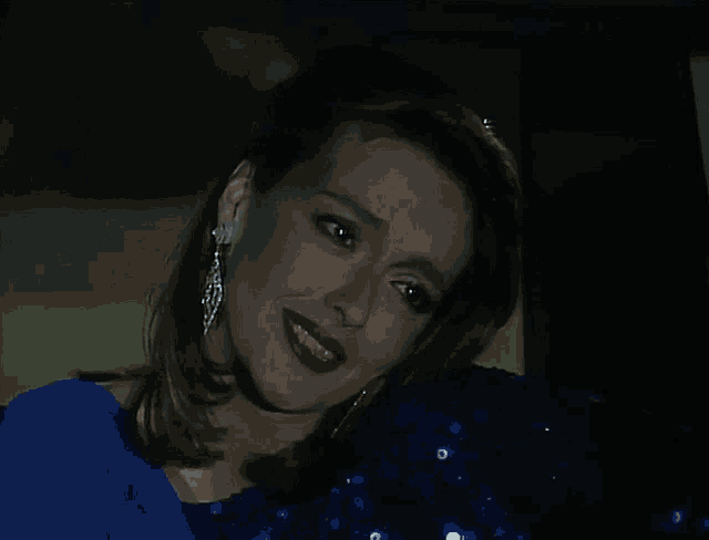 a woman wearing a blue dress and silver earrings smiles