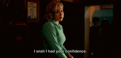 a woman in a green sweater is standing in a dark room and says i wish i had your confidence .