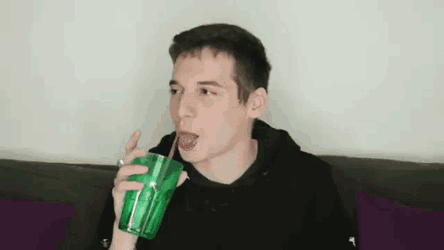 a young man is drinking a drink through a straw from a green cup .