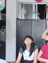 a group of girls are sitting on the floor in a room with a fan in the background .