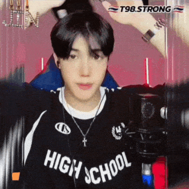 a young man wearing a high school shirt is standing in front of a microphone