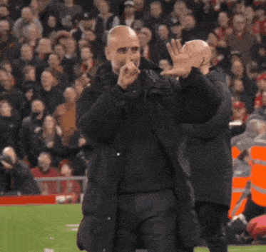 a bald man in a black jacket stands next to another bald man in an orange jacket