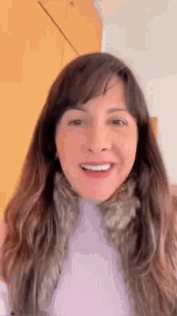 a woman with long hair is smiling and wearing a purple sweater and scarf .