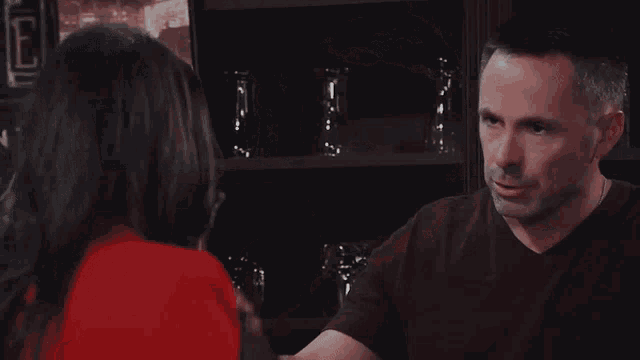 a man and a woman are looking at each other in a room . the woman is wearing a red jacket .