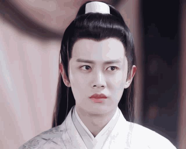 a man with a ponytail and a white shirt looks at the camera