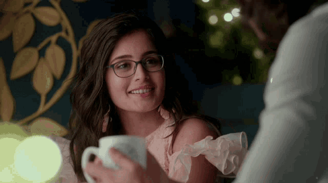 a woman wearing glasses smiles while holding a cup
