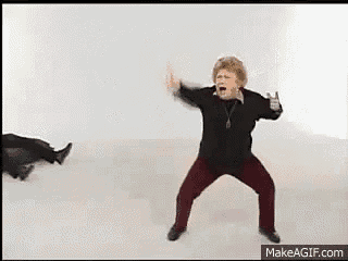 an older woman is dancing in a room with a man laying on the floor behind her .