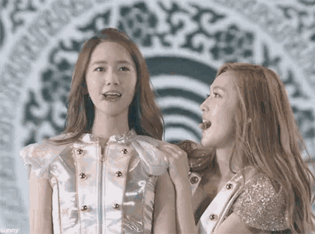 two beautiful young women are standing next to each other on a stage and looking at each other .