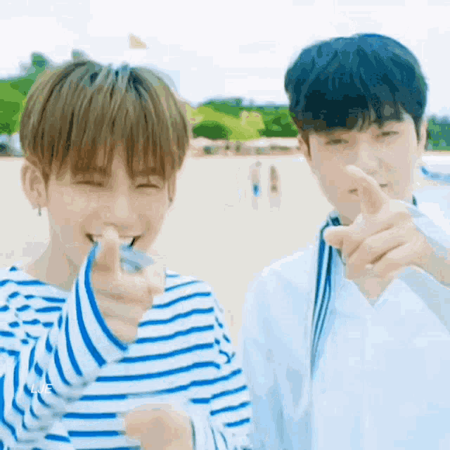 a couple of young men are standing next to each other on a beach and pointing at the camera .