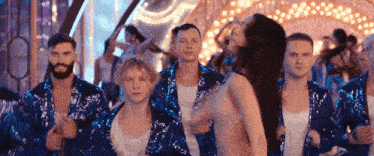 a group of men and women in blue sequined jackets are dancing